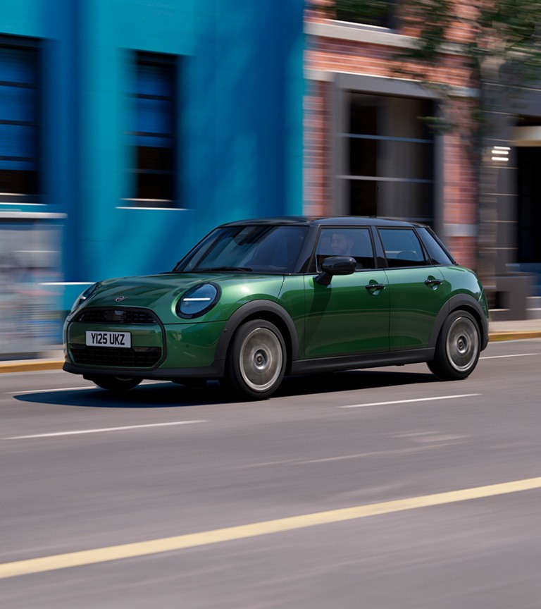 MINI Cooper 5-Door drives swiftly down a city street, passing a bright blue wall and brick building. The scene conveys a sense of speed and urban energy.